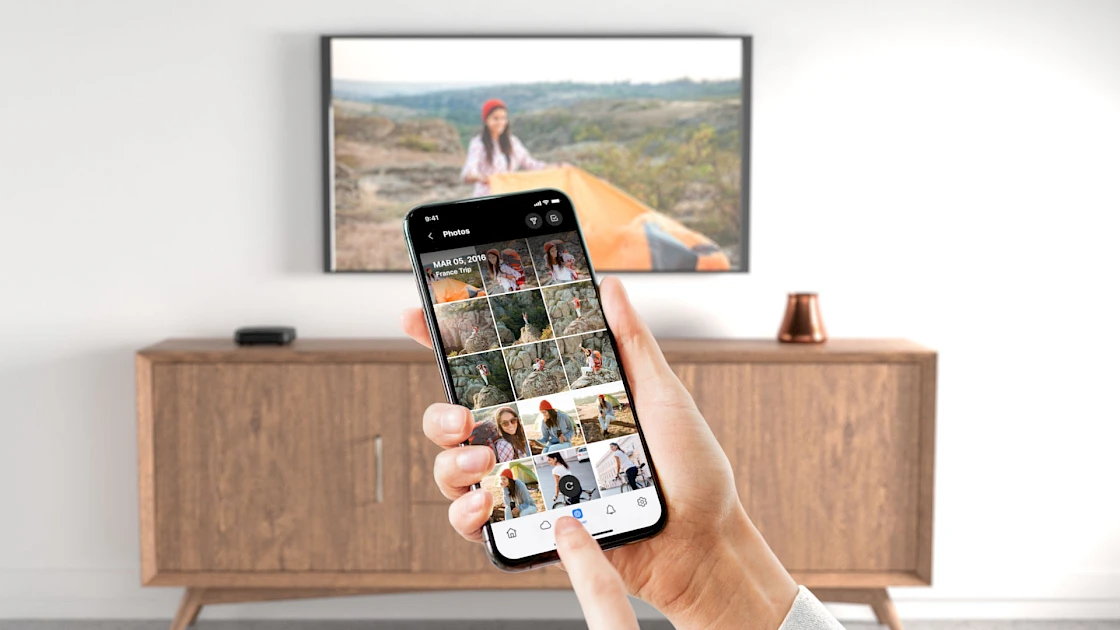 Un telefono in mano che mostra immagini che vengono visualizzate anche su un televisore.