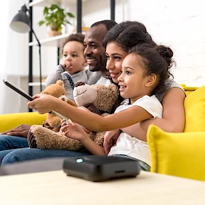 Una familia sentada en un sofá disfrutando de un vídeo con un dispositivo Amber X en primer plano.