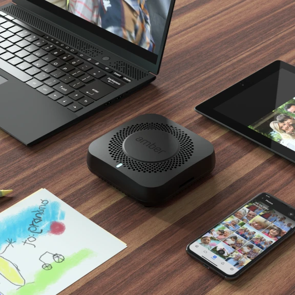 Ein Amber X-Gerät auf einer Tischplatte, umgeben von einem Laptop, einem Telefon und einem Tablet.